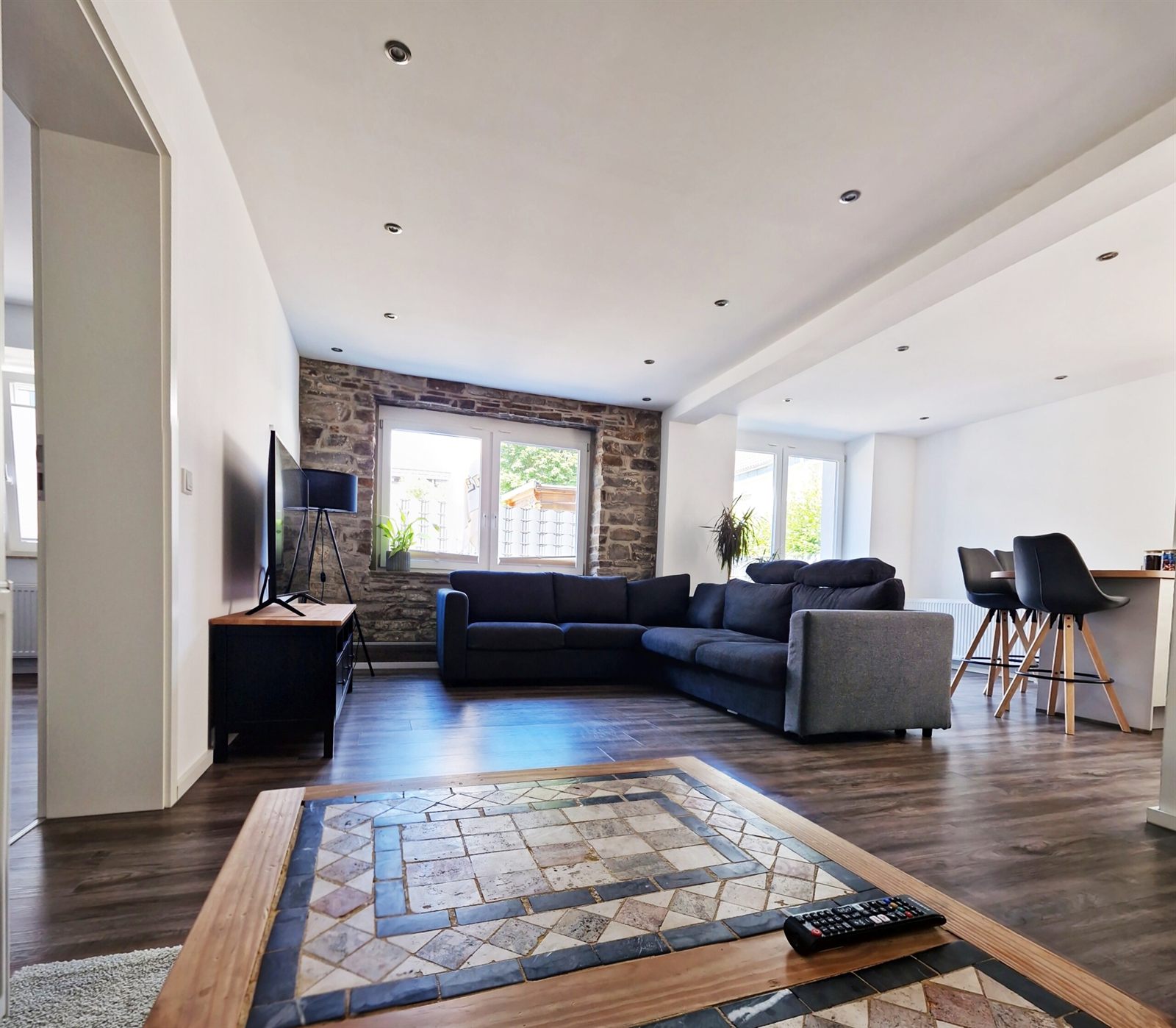 Heller Wohn- und Essbereich der Ferienwohnung Bielstein mit Natursteinwand und großen Fenstern