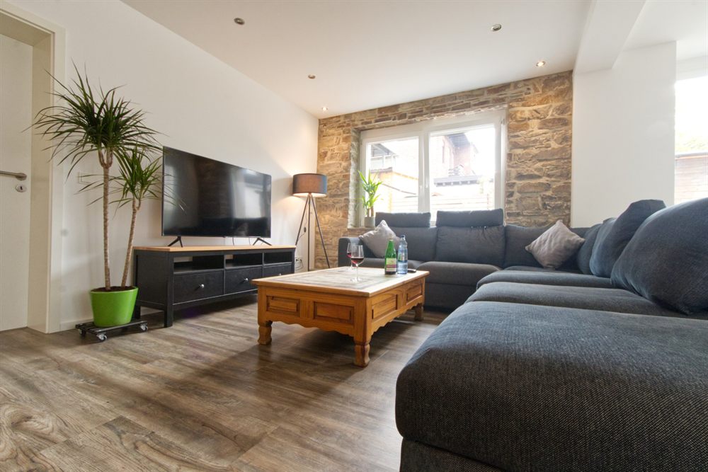 Wohnzimmer der Ferienwohnung Bielstein mit Sofa, Smart-TV und Natursteinwand